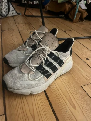Adidas LYXCON 94 sneakers - Säljer ett par Adidas sneakers i beige mocka med svarta detaljer och vita snören. Skorna har de klassiska tre ränderna på sidan och en chunky sula. Tungan har perforerade hål och textdetaljer. Perfekta för dig som gillar streetwear och en sportig look. Nypris när ja köpte dom för ca 6 månader sen var 1490 kr 
