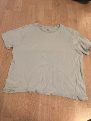 Ljusgrön basic t-shirt - En enkel ljusgrön t-shirt med rund hals och korta ärmar. Perfekt för en avslappnad stil och lätt att matcha med andra plagg. Tillverkad i mjuk bomull för skön komfort. Dock har den en lila fläck som tyvärr inte går bort.