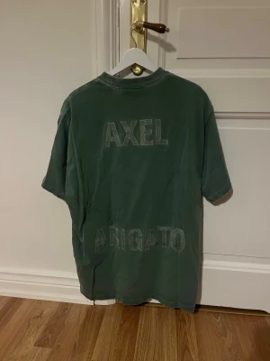 Grön t-shirt från Axel Arigato - Snygg grön t-shirt från Axel Arigato med broderat tryck på ryggen. T-shirten har en avslappnad passform och klassisk rund hals. 