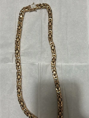 Guldplaterat kejsar halsband - Snyggt halsband i guldfärg med kraftig, flätad kedjedesign. Halsbandet har en unik och detaljerad länkstruktur som ger ett exklusivt intryck. Perfekt för dig som vill sticka ut med ett statement-smycke. Materialet ser ut att vara metall med blank finish.