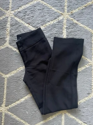 Svarta kostymbyxor med raka ben - Snygga svarta kostymbyxor med raka ben och hög midja. Byxorna har två knappar i linningen och diskret dragkedja. Klassisk och stilren modell som passar till många olika looks. Materialet känns mjukt och följsamt.