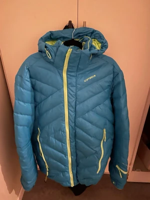 Blå dunjacka från Icepark med huva - Snygg blå dunjacka från Icepark med limegröna dragkedjor och detaljer. Jackan har en fast huva, två sidofickor med dragkedja och en sportig, quiltad design. Perfekt för kalla vinterdagar och håller dig varm med stil.