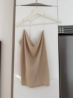 Beige linnetopp med tunna band - Säljer en stilren beige linnetopp med tunna axelband och snygg dr localeffekt framtill. Perfekt för coole sommarkvällar eller när du vill ha en fat fit. Enkel att matcha med jeans eller kjol.