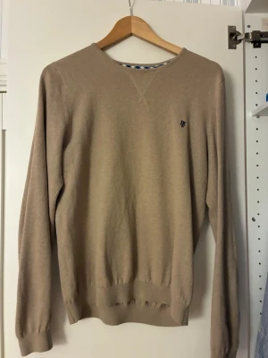 Tjocktröja från Hampton republic - Klassisk beige stickad tröja från Hampton republic med rund halsringning och diskret blå logga broderad på bröstet. Tröjan har långa ärmar och ribbade muddar vid ärmslut och nederkant. Perfekt basplagg till garderoben. Bra skick och inga fläckar. Storlek s-m. Hör av er om de är några funderingar!