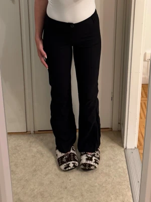 Svarta bootcut byxor med låg midja - Säljer ett par svarta bootcut byxor med låg midja från Bershka i storlek 34(innerbenslängd 78cm och  hela 98cm). De har klassisk knapp och dragkedja framtill och är tillverkade i ett mjukt material(påminner om linnebyxor fast tightare). 