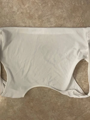 Vit basic body utan ärm - Säljer en enkel vit body i stretchigt material. Bodyn har en klassisk rund halsringning och är ärmlös, perfekt att styla med olika outfits. Materialet känns mjukt och följsamt mot huden.