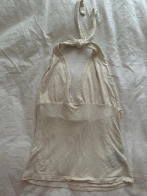 Vit  halterneck linnetopp - Säljer en vit  halterneck linnetopp med djup v-ringning och knyt i nacken. Toppen är ärmlös och har en enkel, stilren design som passar perfekt till sommaren. Materialet känns mjukt och lätt mot huden.