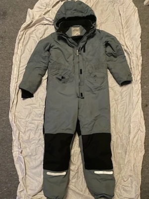 Grå täckoverall från Protech - Täckbyxa overall från Protech i grått med svarta förstärkningar på knäna och reflexdetaljer vid benen. Utrustad med huva, dragkedja framtill och två fickor. Perfekt för kalla dagar och utomhusaktiviteter.