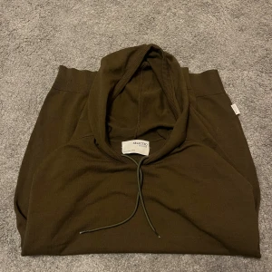 Mörkgrön hoodie från Selected Homme - Snygg mörkgrön hoodie från Selected Homme med klassisk huva och dragsko. Tillverkad i mjukt stickat material som känns skönt mot huden. Hoodien har ribbade muddar vid ärmslut och nederkant för en clean look. Perfekt för dig som gillar stilrena plagg.