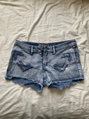 Blå jeansshorts - Säljer ett par blå jeansshorts med fina detaljer. Supersnygga shorts, några stenar har fallit av men det är inte något som märks.