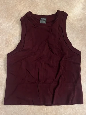 Vinröd ribbad linnetopp från Newbody - Säljer en vinröd ribbad linnetopp från Newbody. Toppen är ärmlös och har en croppad passform som är perfekt för att matcha med höga jeans eller shorts. Materialet är mjukt och stretchigt, vilket gör den bekväm att bära hela dagen.