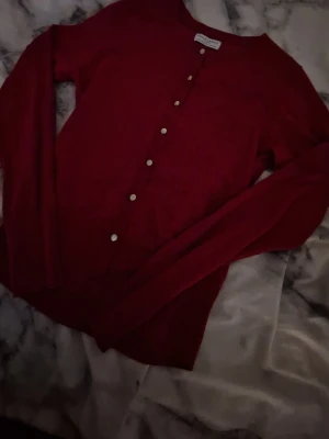 Vinröd kofta med pärlemorknappar - Stilren vinröd kofta från Filippa K med rund halsringning och långa ärmar. Koftan har klassiska pärlemorknappar framtill och är tillverkad i ett mjukt, tunt material som passar perfekt till lager på lager. Enkel och tidlös design.