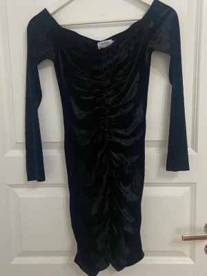 Svart klänning - Säljer en svart långärmad klänning från Flounce London i mjuk sammet. Klänningen har offshoulder-design och snygg rynkning längs hela framsidan som ger en cool och figurnära look. Perfekt för dig som vill sticka ut med en elegant och trendig stil. Aldrig använd 