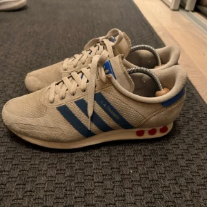 Adidas LA Trainer - Snygga Adidas LA Trainer sneakers i beige med blå ränder och detaljer. Sparsamt använda. Storlek 42 2/3