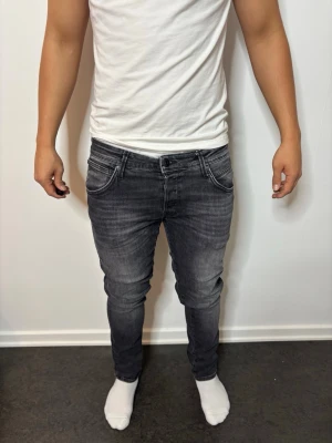 Svart slim fit jeans med slitningar - Säljer ett par grå slim fit jeans med snygga slitningar och tvättad look. Jeansen har klassiska fem fickor, dragkedja och knappstängning. Perfekt för dig som gillar en modern och tight passform.