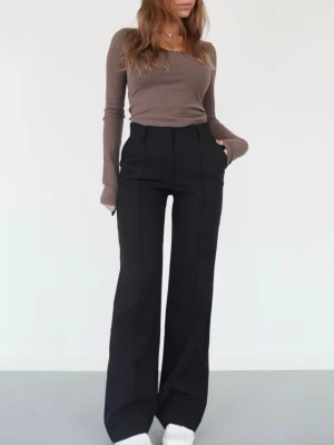 Vida svarta kostymbyxor - Snygga svarta kostymbyxor med hög midja och vida ben. Byxorna har pressveck framtill och sidfickor för en clean look. Perfekta för dig som gillar en stilren och trendig outfit.