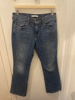 Blå bootcut jeans från Levi's - Säljer ett par klassiska blå bootcut jeans från Levi's med fyra fickor och snygga detaljer på bakfickorna. Jeansen har en lätt tvättad look och är tillverkade i slitstark denim. Perfekta för dig som gillar en tidlös och avslappnad stil.