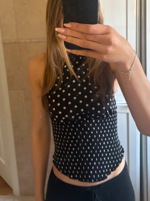 Svart prickig ärmlös topp - Snygg svart ärmlös topp med vita prickar i olika storlekar. Toppen har hög hals och figurnära passform med vågig kant nertill. Perfekt för dig som gillar trendiga och lekfulla mönster. Materialet känns mjukt och stretchigt. Aldrig använd endast testad💕