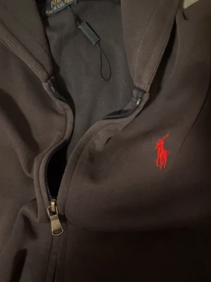Mörkblå hoodie från Polo Ralph Lauren - Snygg mörkblå hoodie från Polo Ralph Lauren med dragkedja och klassisk röd logga broderad på bröstet. Hoodien har huva och är tillverkad i mjukt bomullsmaterial. Perfekt för en avslappnad och stilren look. Pris kan diskuteras 
