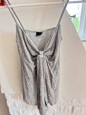 Grå linnetopp med knyt framtill - Säljer en grå linnetopp från Bik Bok med smala axelband och snygg knyt-detalj framtill. Toppen är ärmlös och har en avslappnad passform, perfekt för varma dagar. Materialet känns mjukt och lätt mot huden.