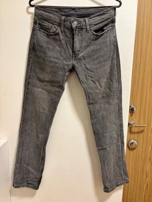 Grå Levi's jeans med rak passform - Säljer ett par grå jeans från Levi's med klassisk rak passform. Jeansen har fem fickor, bälteshällor och Levi's ikoniska läderpatch bak i midjan. Tillverkade i denim med snygg tvättad look och subtila slitningar. Perfekta för en avslappnad stil.