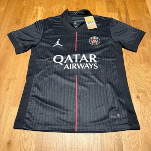 PSG 4th kit 25/26 X O.Dembele  - Snygg svart PSG matchtröja med O. Dembélé och nummer 10 på ryggen. Tröjan har Qatar Airways-tryck på bröstet, PSG-logga och Jordan-logga. Tillverkad i lätt och ventilerande material, perfekt för fotboll eller träning. Röd detalj framtill och korta ärmar.