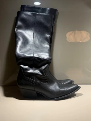 Svarta cowboy boots i skinn - Säljer ett par svarta cowboyboots i mjuk skinnimmitation med spetsig tå och låg klack. 
