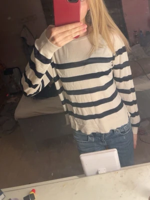 Randig beige och marinblå tröja - Säljer en snygg beige tröja med marinblå horisontella ränder. Tröjan har rund halsringning och långa ärmar. Perfekt till jeans för en avslappnad look. Materialet känns mjukt och lätt, passar året runt.