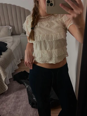 Ljus prickig blus med volanger - Säljer en ljus, transparent blus med prickigt mönster och flera volanglager. Blusen är kortärmad och har en croppad passform som ger en trendig look. Perfekt inför sommaren! 