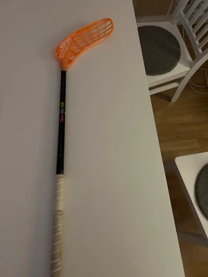 Innebandyklubba Zone svart/orange - Säljer en innebandyklubba från Zone med svart skaft och orange blad. Skaftet har färgglada detaljer. Bladet är helt nytt, aldrig använt bara vinklat. Klubban har gått av men funkar nu ändå som vanligt. 94cm lång