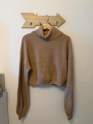 Beige stickad polotröja från NA-KD - Säljer en beige stickad polotröja från NA-KD. Tröjan har en croppad passform, bred polokrage och långa ärmar. Materialet är tjockt och ribbstickat vilket gör den extra mysig och trendig till hösten och vintern.