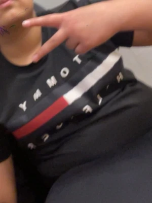 Svart Tommy Hilfiger t-shirt - Snygg svart t-shirt från Tommy Hilfiger med det klassiska logotrycket i vitt, rött och blått över bröstet. T-shirten har korta ärmar och en normal passform. Perfekt för dig som gillar stilrena och ikoniska plagg.