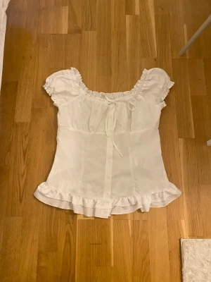 Vit kortärmad blus med volang - Vit blus med korta puffärmar, knappar framtill och volangkant nedtill. 