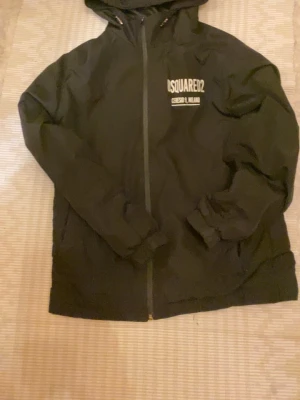 Svart vindjacka från Dsquared2 - Snygg svart vindjacka från Dsquared2 med huva och dragkedja framtill. Jackan har vit logga och texten 'Ceresio 9, Milano' tryckt på både bröstet och ryggen. Tillverkad i lätt material som passar perfekt för blåsiga dagar. Sportig och trendig design.