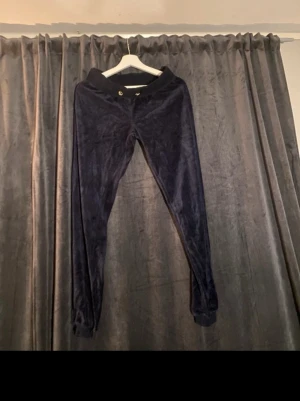 Marinblå cubus set - Mörkblå byxor och hoodie i mjukt material med resår i midjan och guldfärgad knapp framtill. Byxorna har smal passform och är perfekta för en avslappnad och trendig stil. Materialet är glansigt och ger en lyxig känsla. Byxor som nya tröjan lite urtvättad