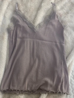 Ljuslila ribbad linnetopp från Amisu/ new yorker - Supersöt ljuslila ribbad linnetopp från Amisu med spetsdetaljer vid v-ringad hals och tunna axelband. Toppen har en croppad känsla och vågig kant nedtill, perfekt för att lyfta vilken outfit som helst.