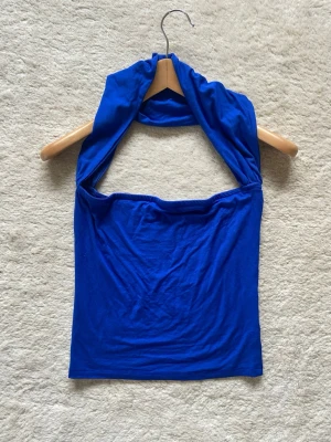 Blå halterneck tubtopp - Snygg blå halterneck tubtopp i mjukt stretchigt material. Toppen är ärmlös och har en bandeauformad passning med breda band som är runt nacken. 