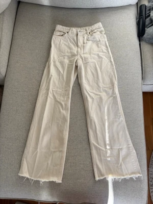 Vida beiga jeans  - Säljer ett par trendiga vita jeans med hög midja och vida ben från Monki. Jeansen har råa, fransiga benslut och klassisk femficksmodell. Perfekta för dig som gillar en avslappnad och modern stil. Materialet är bomull och de har en ljus tvätt. Storlek  24 i midjan. Passat mig när jag var XS så antar att det motsvarar. Aldrig använda, endast provade. De är beiga/creme färgade. Hög midja