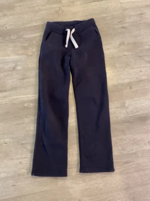 Mörkblå mjukisbyxor   - Mörkblå mjukisbyxor från Russemerch med lite utsvängda ben och vita snören. Byxorna har två fickor fram och är gjorda i ett mjukt, fleeceliknande material som känns riktigt skönt mot huden. Perfekta för chill dagar eller när du vill vara extra bekväm. 