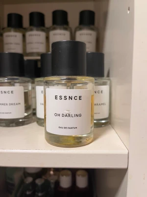 ESSNCE Oh Darling Eau de Parfum - ESSNCE Oh Darling Eau de Parfum i en stilren, rund glasflaska med svart lock. Parfymen har en gyllene vätska och minimalistisk vit etikett med svart text. Perfekt för dig som gillar moderna och enkla designer.