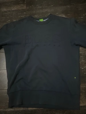 Mörkblå sweatshirt från Hugo Boss - Snygg mörkblå sweatshirt från Hugo Boss med diskret broderad logga på bröstet. Tröjan har rund halsringning, ribbade muddar vid ärmslut och nederkant samt en relaxed fit. Perfekt för en stilren och avslappnad look. Hör av er vid funderingar eller släng iväg ett prisförslag!