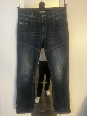 Mörkblå jeans från Pearson - Säljer ett par mörkblå jeans från Pearson med snygga slitningar och kontrastsömmar. Jeansen har fem fickor, raka ben och coola detaljer på knäna samt bakfickor med unik design. Perfekta för en avslappnad och trendig stil. Hör av er vid frågor! W32 L32.