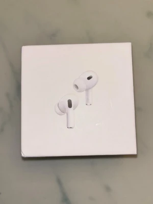 Apple AirPods Pro trådlösa hörlurar - Säljer ett par vita Apple AirPods Pro med laddningsetui och USB-C kabel. Hörlurarna har in-ear design, silikonproppar och stilren form. Perfekta för dig som vill ha grymt ljud och smidig anslutning till din iPhone eller andra Apple-enheter.