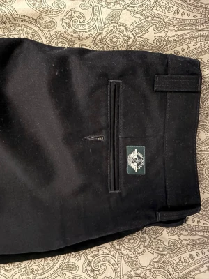 Svarta kostymbyxor från Dockers - Snygga svarta kostymbyxor från Dockers med rak passform. Byxorna har en klassisk look med fickor bak, bälteshällor och en diskret logga ovanför bakfickan. Perfekta för en stilren och clean outfit.