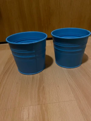 Två blå småhinkar - Säljer två stycken runda små blå metallhinkar. Har använts för att förvara massa pennor. Saknar handtag och skulle kunna användas som krukor om man vill!