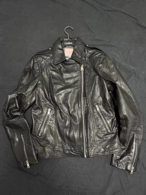 Svart skinnjacka från Gulins - Snygg svart skinnjacka i 100% lammnappa från Livelo women. Jackan har sneddragkedja, två framfickor med dragkedja och detaljerade sömmar. Klassisk bikerstil med krage och dragkedjor vid ärmsluten. Perfekt för en cool och tidlös look.