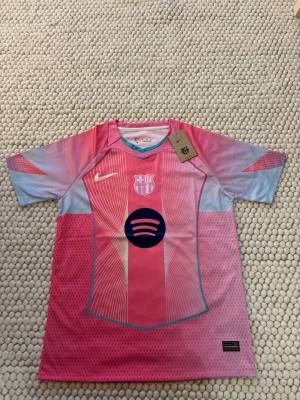 Barça matchtröja rosa/blå Nike - Säljer en FC Barcelona matchtröja från Nike i rosa och ljusblått med klubbmärke och Spotify-logga på bröstet. Tröjan har korta ärmar, sportig passform och är tillverkad i ett lätt, ventilerande material perfekt för träning eller match.
