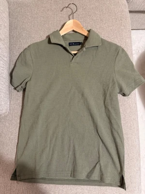 Olivgrön pikétröja  - Snygg olivgrön pikétröja från S.C. Wörishöffer med klassisk krage och korta ärmar. Tillverkad i mjuk bomull som känns skön mot huden. Perfekt till jeans eller shorts för en avslappnad look.