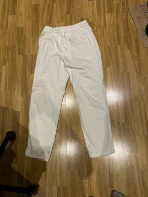 Vita byxor från Zara - Säljer ett par vita linnebyxor kombinerat med jeans från Zara med dragsko i midjan och avslappnad passform. Byxorna har resår i midjan och raka ben, perfekta för kalla sommardagar. Material är som jeans och linne kombinerat.