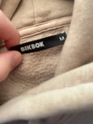 Beige hoodie från BikBok med huva - Säljer en beige hoodie från BikBok i storlek M. Hoodien har en klassisk huva med dragsko, magficka och ribbade muddar. Materialet är mjukt och insidan är fleecefodrad för extra komfort. Perfekt för en chill och avslappnad stil.